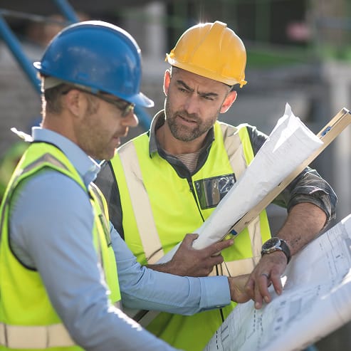 Two construction workers in hard hats and vests reviewing blueprints on-site for TOFCON